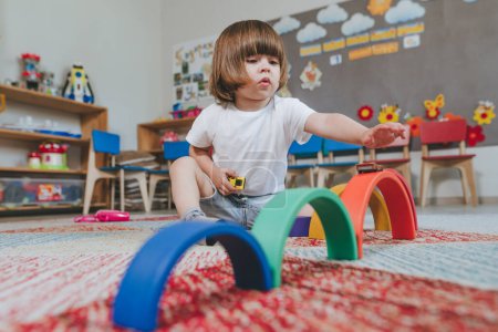 Téléchargez les photos : Little boy playing with rainbow wooden toy sitting on the floor in kindergarten. Selective focus. - en image libre de droit