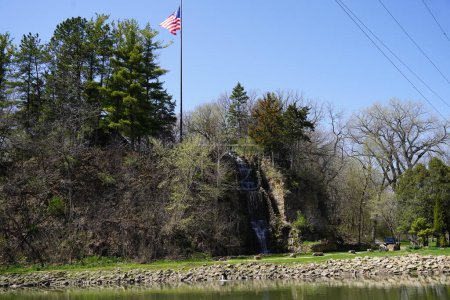 Foto de Ondas de bandera americana en el viento en la cima de la ladera de la montaña con cascada. - Imagen libre de derechos