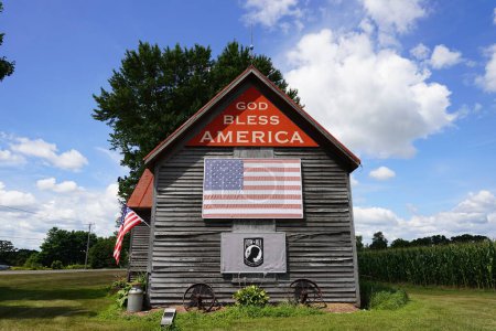 Foto de Green Lake, Washington, Estados Unidos - 16 de mayo de 2020: La antigua casa de madera abandonada se encuentra en el campo de Green Lake, Wisconsin, promoviendo Dios bendiga a América. - Imagen libre de derechos