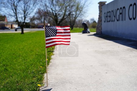 Foto de Pequeñas olas de bandera americana en el viento mostrando orgullo y recuerdo para los veteranos caídos en el sitio conmemorativo del veterano del condado de Sheboygan. - Imagen libre de derechos