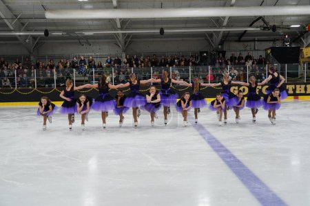 Foto de Mosinee, Wisconsin, Estados Unidos - 26 de febrero de 2021: Mujeres jóvenes en hermosos vestidos púrpuras sincronizadas patinando juntas en la competencia de patinaje sobre hielo de los juegos de invierno de Badger State. - Imagen libre de derechos