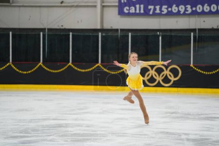 Foto de Mosinee, Wisconsin, EE.UU. - 26 de febrero de 2021: Una joven adulta con un hermoso vestido amarillo participó en la competencia de patinaje sobre hielo de los juegos de invierno de Badger State. - Imagen libre de derechos