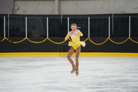 Photo for Mosinee, Wisconsin USA - February 26th, 2021: Young adult female in a beautiful yellow dress participated in badger state winter games ice skating competition - Royalty Free Image