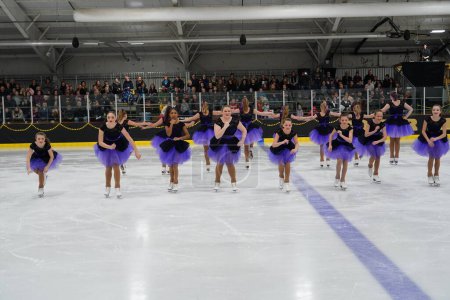 Foto de Mosinee, Wisconsin, Estados Unidos - 26 de febrero de 2021: Mujeres jóvenes en hermosos vestidos púrpuras sincronizadas patinando juntas en la competencia de patinaje sobre hielo de los juegos de invierno de Badger State. - Imagen libre de derechos