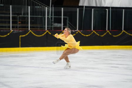 Photo for Mosinee, Wisconsin USA - February 26th, 2021: Adult female in a beautiful yellow dress participated in badger state winter games ice skating competition - Royalty Free Image
