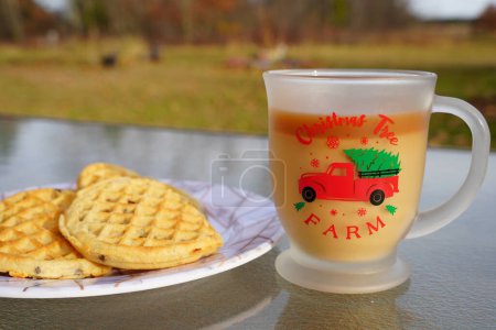 Foto de Taza de café de Navidad de cristal con café y crema junto a un plato de gofres de chispas de chocolate. - Imagen libre de derechos