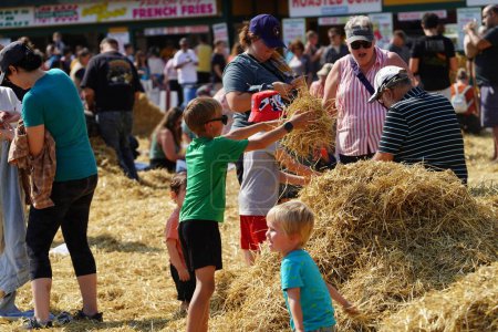 Photo for Milwaukee, Wisconsin USA - September 30th, 2023: Family members gathering together at the Wisconsin State Fair for Harvest Fair festival to create scarecrows out of hay. - Royalty Free Image
