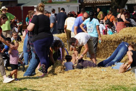 Photo for Milwaukee, Wisconsin USA - September 30th, 2023: Family members gathering together at the Wisconsin State Fair for Harvest Fair festival to create scarecrows out of hay. - Royalty Free Image