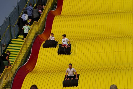Photo for Milwaukee, Wisconsin USA - October 1st, 2023: Family members use burlap sacks to slide down a giant yellow slide at the Wisconsin State Fair. - Royalty Free Image