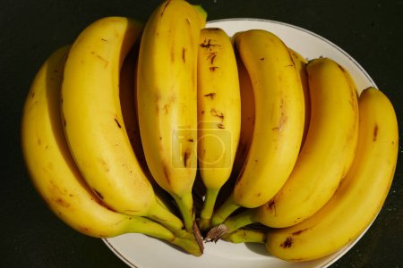 Téléchargez les photos : Un groupe de bananes mûres assis sur une table à l'extérieur prêt à être servi. - en image libre de droit