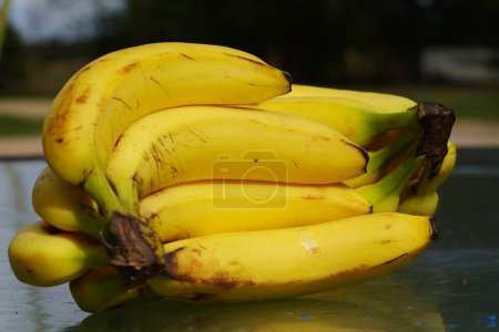Téléchargez les photos : Un groupe de bananes mûres assis sur une table à l'extérieur prêt à être servi. - en image libre de droit