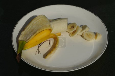 Téléchargez les photos : Banane jaune pelée et tranchée assise sur une assiette prête à être mangée. - en image libre de droit