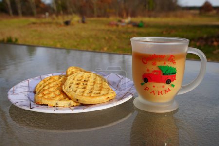 Foto de Taza de café de Navidad de cristal con café y crema junto a un plato de gofres de chispas de chocolate. - Imagen libre de derechos