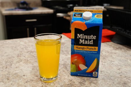 Téléchargez les photos : Fond du Lac, Wisconsin États-Unis - 15 février 2024 : Grand carton de jus de mangue Minute Maid Punch aromatisé se trouve à côté d'un verre clair de jus d'orange. - en image libre de droit
