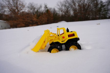 Yellow kids front loader construction toy sits out in the snow during the winter season.