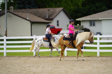 Photo for Fond du Lac, Wisconsin / USA - July 17th, 2019: Young girls riding around on horses on a public horse ranch field in Fond du Lac, Wisconsin - Royalty Free Image