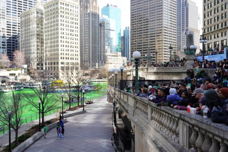 Photo for Chicago, Illinois USA - March 16th, 2024: Spectators dressed in St. Patrick colors and costumes stood and watched the Green color dyeing of the Chicago River standing in front of the Trump building - Royalty Free Image
