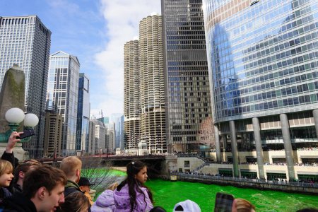 Foto de Chicago, Illinois, EE.UU. - 16 de marzo de 2024: Los espectadores vestidos con colores y trajes de San Patricio se pararon y observaron el teñido de color verde del río Chicago frente al edificio Trump. - Imagen libre de derechos
