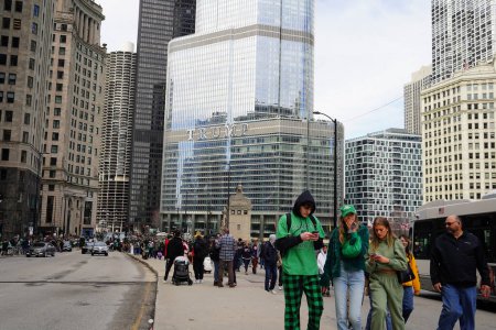 Photo for Chicago, Illinois USA - March 16th, 2024: Spectators dressed in St. Patrick colors and costumes stood and watched the Green color dyeing of the Chicago River standing in front of the Trump building - Royalty Free Image