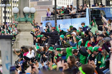 Téléchargez les photos : Chicago, Illinois États-Unis - 16 mars 2024 : Des spectateurs vêtus de couleurs et de costumes de St. Patrick se tenaient debout et regardaient la teinture de couleur verte de la rivière Chicago debout devant le bâtiment Trump - en image libre de droit