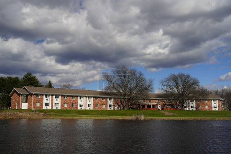 Foto de Mauston, Wisconsin, EE.UU. - 13 de abril de 2024: vista panorámica de los edificios de apartamentos de ladrillo al lado de un lago durante un día nublado. - Imagen libre de derechos