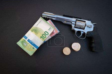 Téléchargez les photos : À côté d'une liasse d'argent et d'une pile de pièces d'or Krugerrand se trouve un revolver - en image libre de droit
