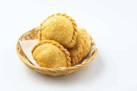 Curry puff on wicker basket isolated on white background. Samosa chicken fried curry dumpling,  meat or vegetable snuffing. Yummy pie, Asian street food, Crispy snack for eating with coffee tea bread