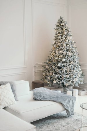 Téléchargez les photos : Décor de Noël dans un studio photo en gris et blanc. Arbre de Noël blanc neige, cadeaux et lanternes, canapé. Hors de propos. Place pour une séance photo - en image libre de droit