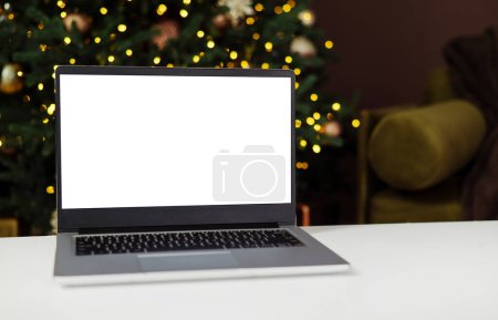 Téléchargez les photos : Vue de face de l'ordinateur portable avec écran blanc à la maison avec arbre de Noël lumière chaude. Rabais de Noël. Achats en ligne. Cadeaux pour la nouvelle année et Noël - en image libre de droit