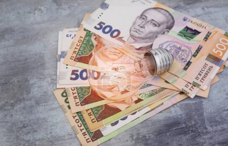 Téléchargez les photos : L'argent ukrainien hryvnias et une ampoule. Le concept d'augmentation des prix de l'électricité en Ukraine et le déficit. Coûts d'électricité. - en image libre de droit