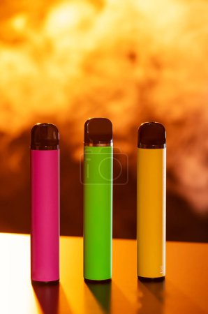 A set of colorful disposable electronic cigarettes of different shapes on a black background with smoke. Concept of modern smoking, vaping and nicotine