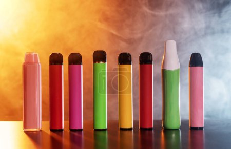A set of colorful disposable electronic cigarettes of different shapes on a black background with smoke. Concept of modern smoking, vaping and nicotine