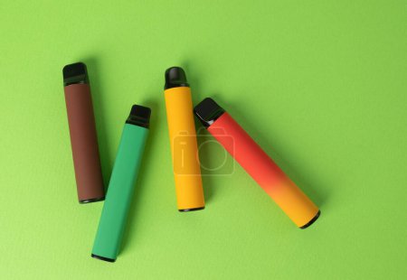 Téléchargez les photos : Ensemble de cigarettes électroniques jetables colorées sur un fond vert. Le concept de tabagisme moderne. Vue du dessus - en image libre de droit