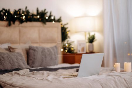 Téléchargez les photos : Ordinateur portable ouvert couché sur le lit dans la chambre avec décorations de Noël décorées à la maison. Concept freelance. Photo de haute qualité - en image libre de droit