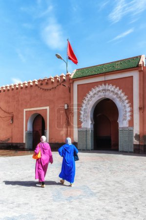 Téléchargez les photos : Femmes en jellaba colorée et fluide, passant devant une porte ouverte à Marrakech, Maroc - en image libre de droit