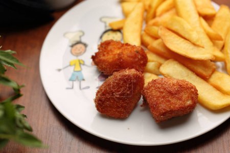 Chicken nuggets with potato fries, on a white plate, top view. Lunch, child portion, selective focus. Breaded chicken, meat pieces, served with handmade chips.