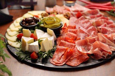 Appetizers buffet with meat and cheese snacks, dates and pickles on wooden table, close-up. Cheese and cold cuts board, tapas. Party snacks set.