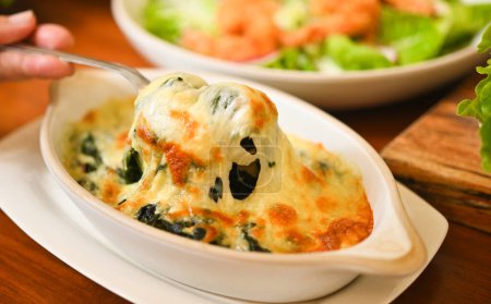 Photo for Baked spinach with cheese in a hot ceramic bowl on a wooden table - Royalty Free Image