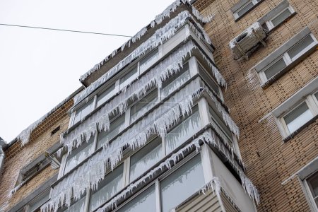 Overhanging Icicles on Apartment Building Facade. Stalactite-like icicles descend from the overhang of an apartment buildings windows and eaves.