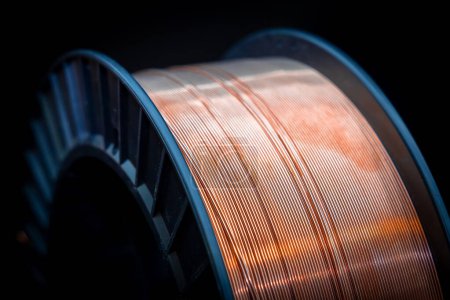 Black plastic spool with shiny copper wire. Shiny copper wire wound on a reel, dark background, close-up. Electronics and industrial equipment.