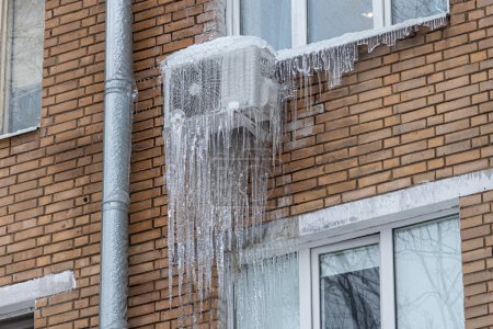 Eiszapfen hängen an einer Klimaanlage an einem Backsteingebäude. Gefrorene Klimaanlage mit Eiszapfen.