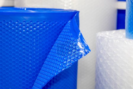 Eine Rolle blauer Luftpolsterfolie vor einem Hintergrund aus anderen Verpackungsmaterialien. Diese Art von Verpackung wird verwendet, um empfindliche Gegenstände während des Transports zu schützen.