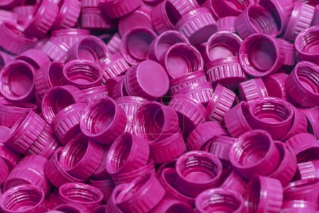 Foto de Producción industrial de tapones de botellas de polietileno púrpura de alta densidad. Una pila de tapas de botellas de plástico de HDPE púrpura recién fundido. Producción de envases de bebidas. - Imagen libre de derechos