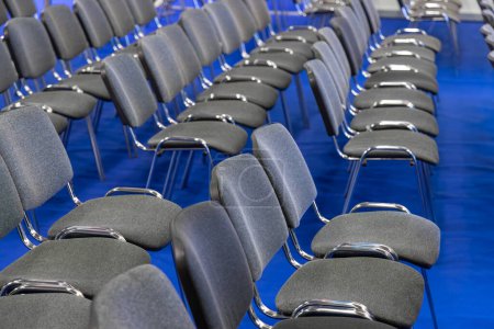 Téléchargez les photos : Tableau symétrique de chaises de conférence grises sur tapis bleu. Organisation de sièges pour des événements et des séminaires d'entreprise. Chaises vides en attente d'une assemblée ou d'une présentation. - en image libre de droit