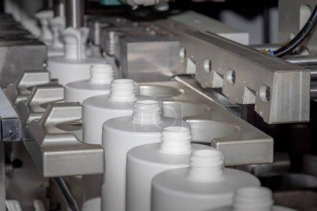 Foto de Línea de producción automatizada para colada de botellas de plástico blanco. Botellas de plástico blanco en una línea de producción. Moldeo de botellas de plástico blanco. Embalaje líquido. - Imagen libre de derechos