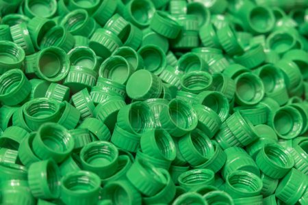 Foto de Producción industrial de tapones de botellas de polietileno verde de alta densidad. Una pila de tapas de botellas de plástico de HDPE verde recién moldeado. Producción de envases de alimentos. - Imagen libre de derechos