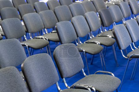 Perfekt ausgerichtete graue Stühle auf blauem Teppich für Seminare. Moderne graue Sitzordnung für Firmenkonferenzen. Bereit für Teilnehmer: Sleek Chair Setup in einer Business-Event-Halle.