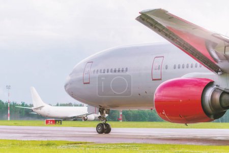 The planes lined up on the taxiway, awaiting clearance from the control tower. The main character of the photo, an airplane with a bright red engine, demonstrates the scale of aircraft technology.