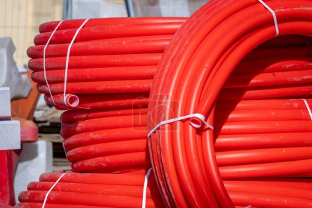 Photo for Coils of red polyethylene pipes for laying high voltage electrical cables underground. Construction site with city. Red pipes rolled into rings or coils. Electrical insulation. - Royalty Free Image