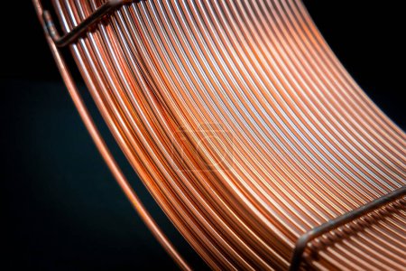 Elegantly curved copper wires on dark background, industrial beauty. Coil of thick copper wire, close-up. Electrical components and conductors.